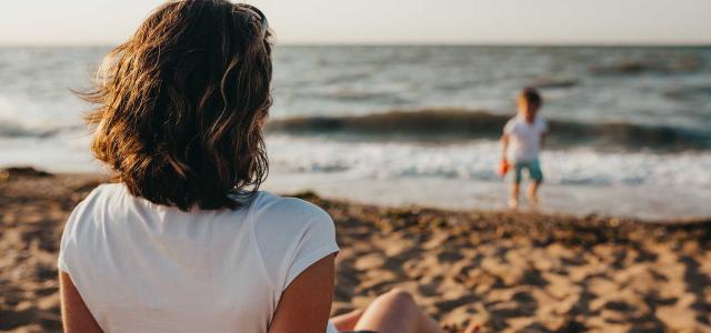 Women on beach staring at child in ocean.